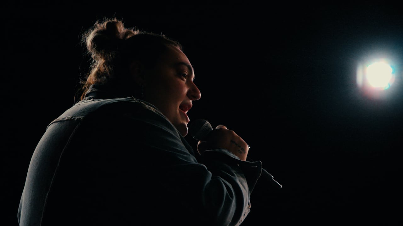 A woman with a top knot sings into a microphone