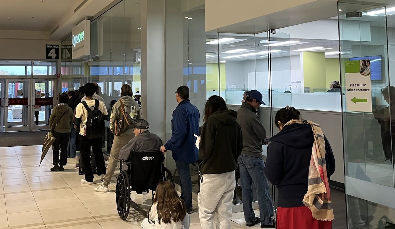 A long line of people wait outside a lab centre with a storefront inside a mall