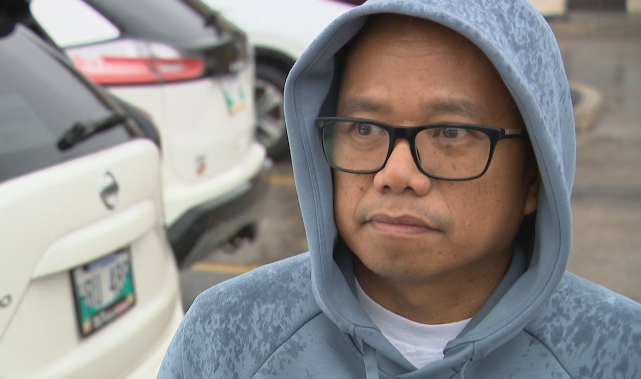 A man with glasses wears a blue hooded sweatshirt soaked with rain on an overcast day