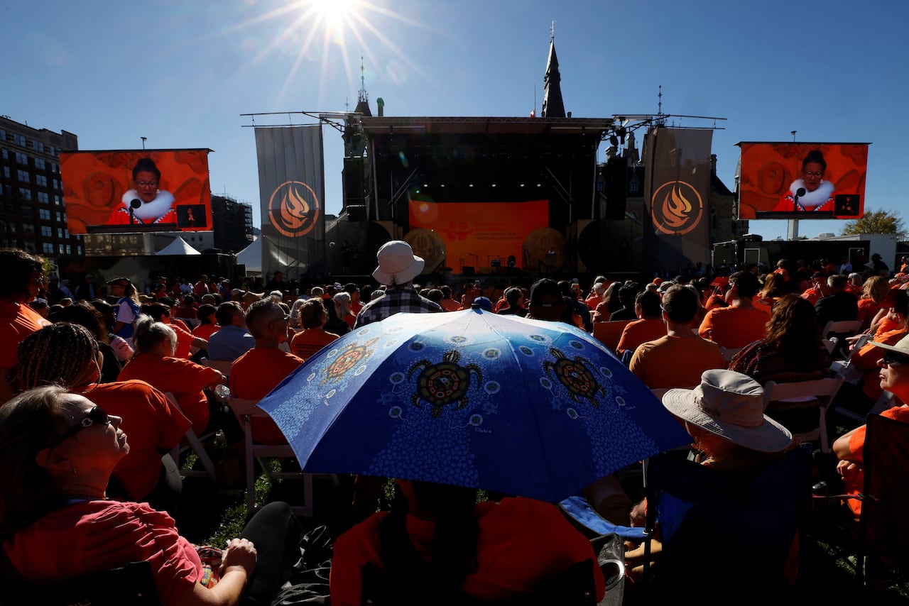 People, many of them wearing orange, attend a gathering on a legislature lawn.