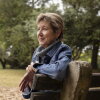 Vicky Stinson, a youthful looking 65-year-old, is pictured in profile, sitting on a part bench.