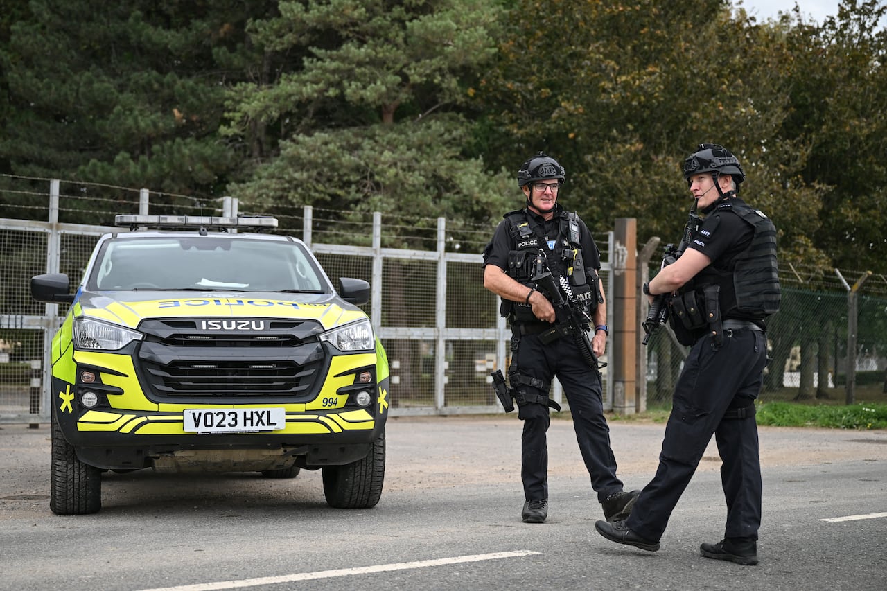 Two police officers stand near a car at a gated entrance.