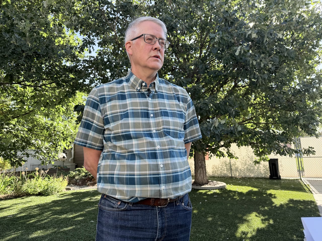 A man stands in a grassy backyard.
