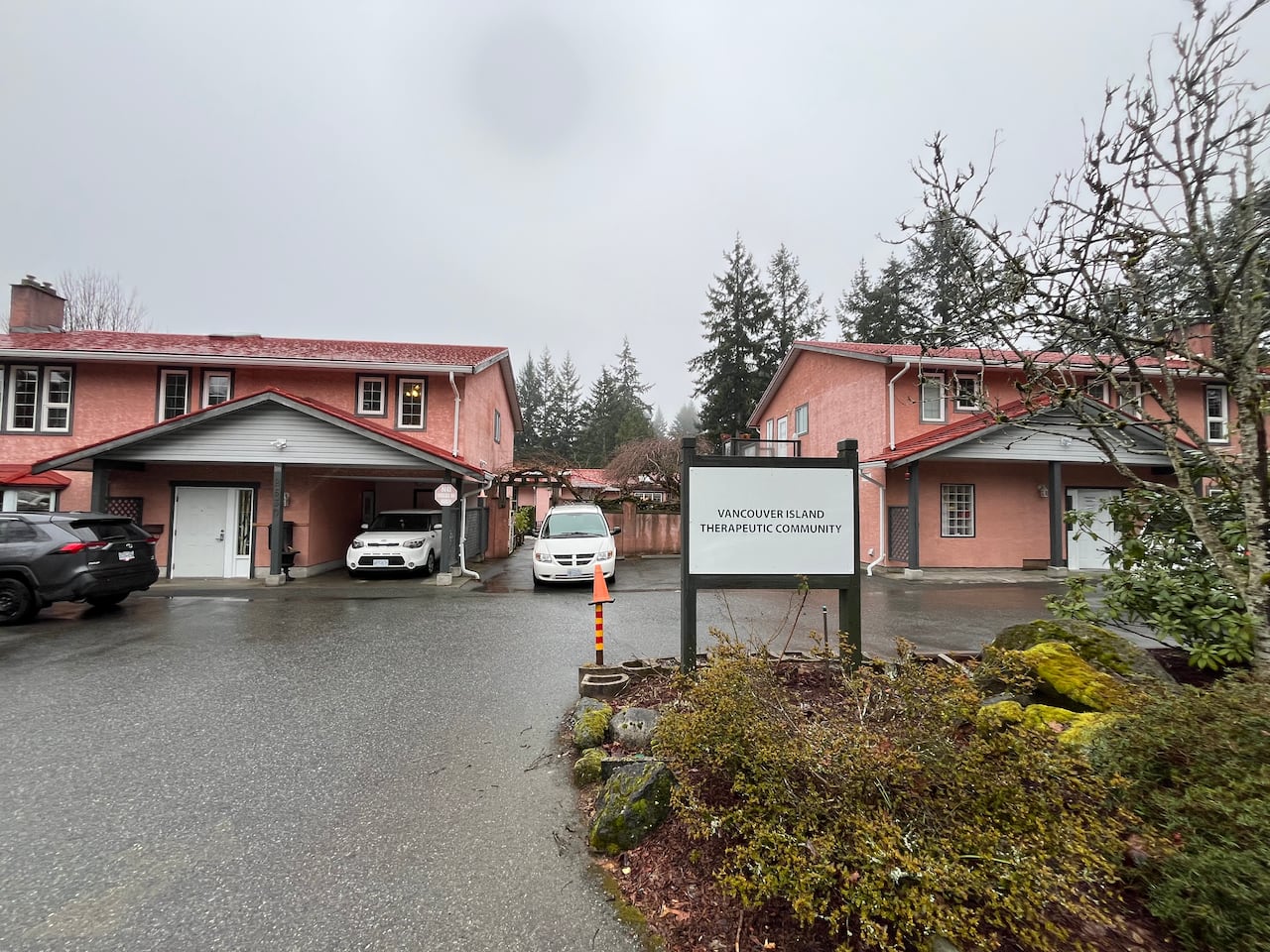 A pair of pink houses appear behind a sign that reads Vancouver Island Therapeutic Community.