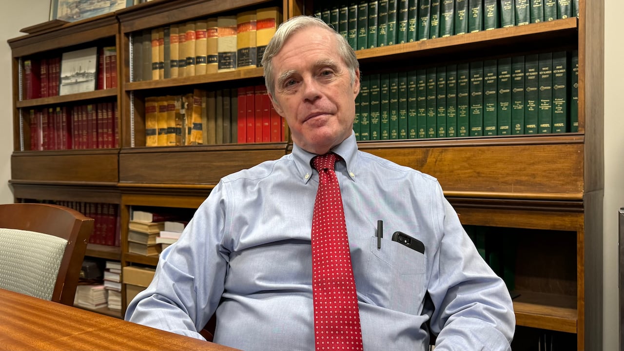 Tim Woodcock sits at a table with shelves of books in the background.