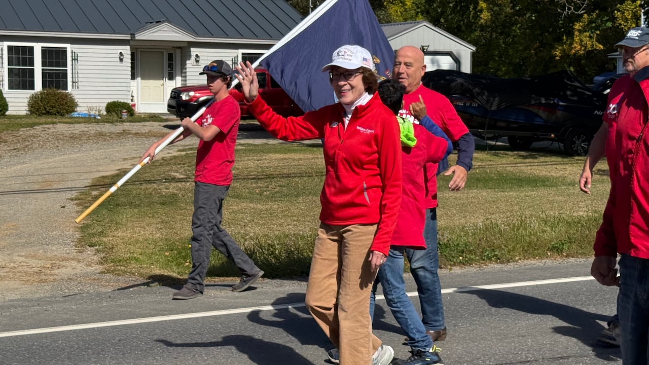 Susan Collins waves as she walks along a road.