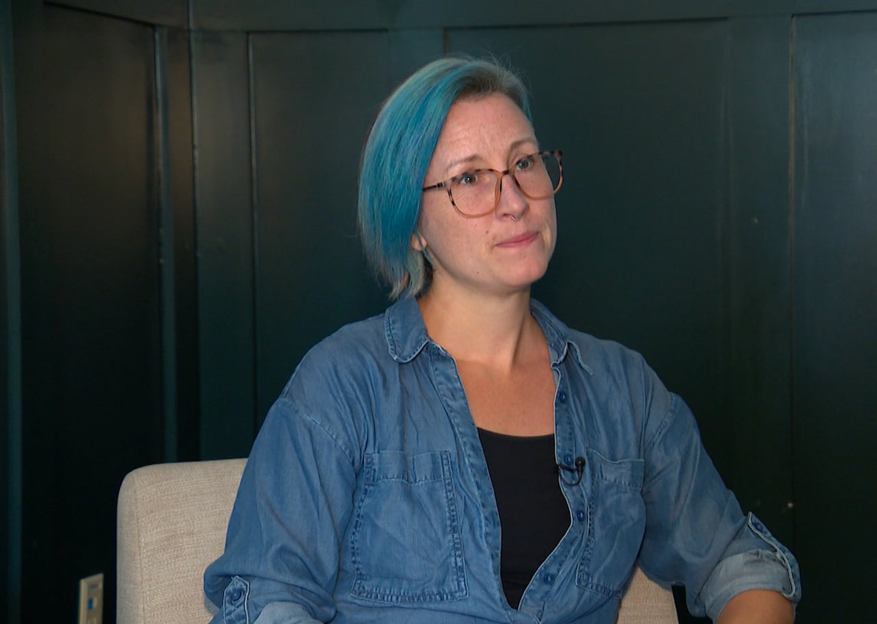 A woman in a blue button-up top sits on a couch.