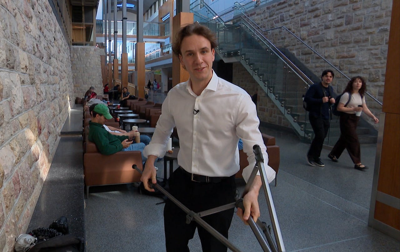 A man in a white button-up shirt holds a tripod.