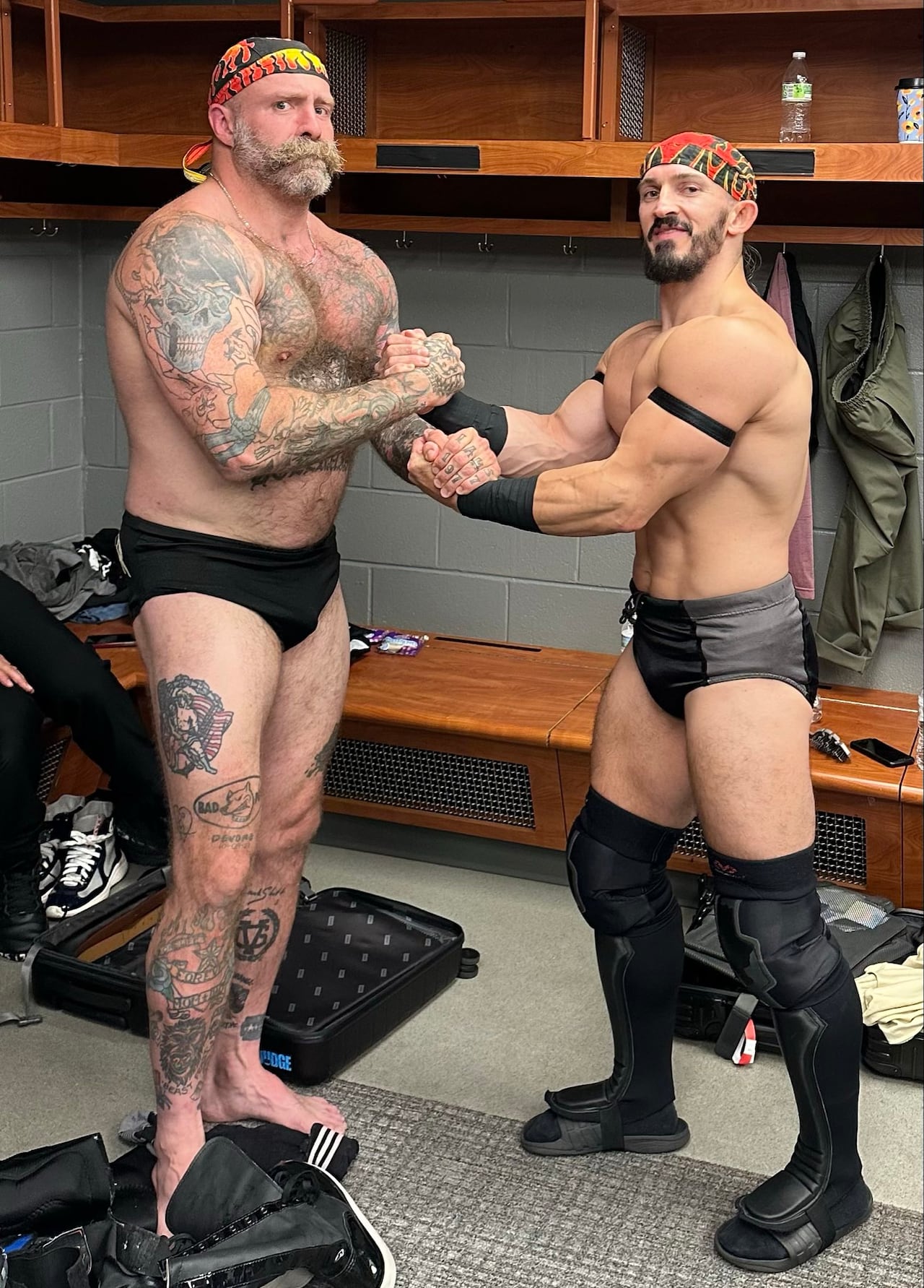 Photo of two muscular men posing together in a locker room.