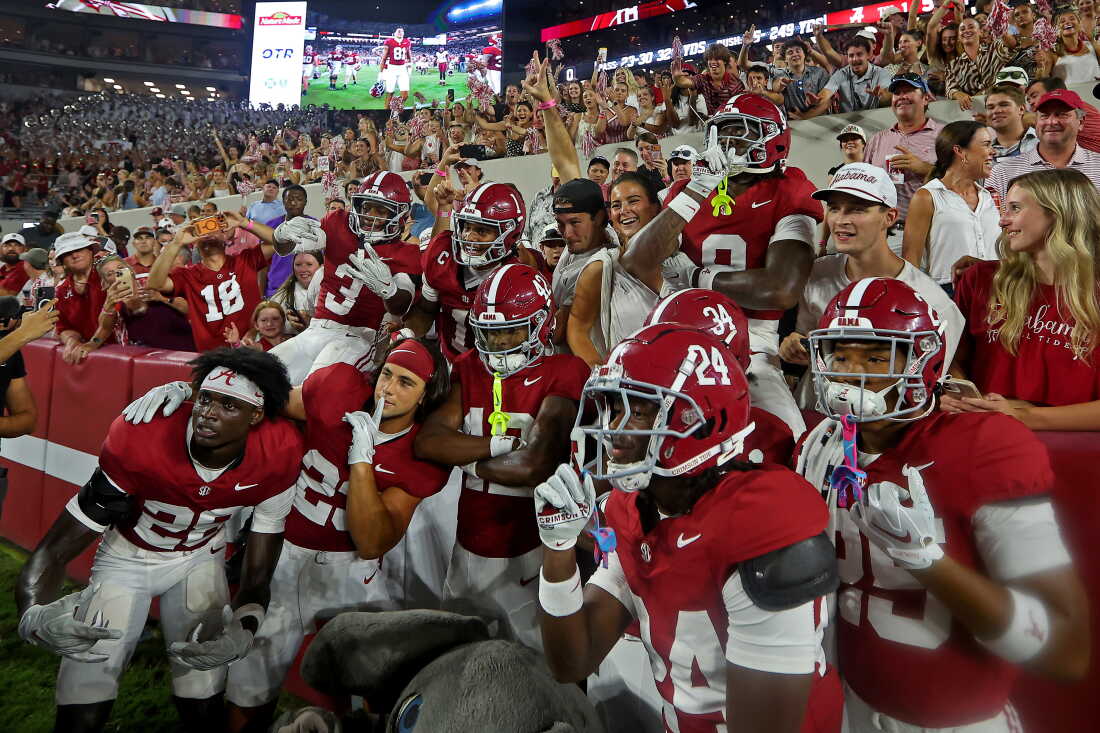 Alabama Crimson Tide football players, wearing white pants, red tops and red helmets, pose with fans on September 19.