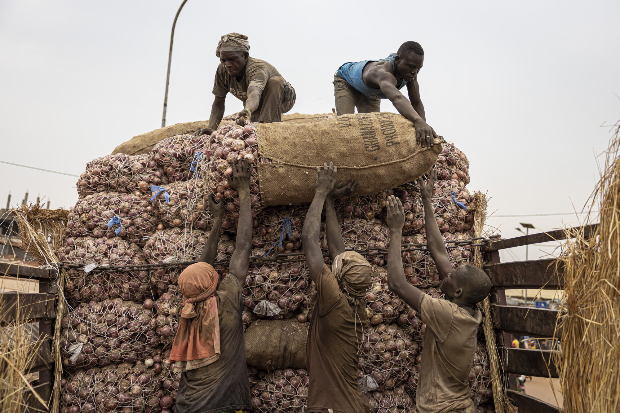 Workers unload a truck containing bags full of onions