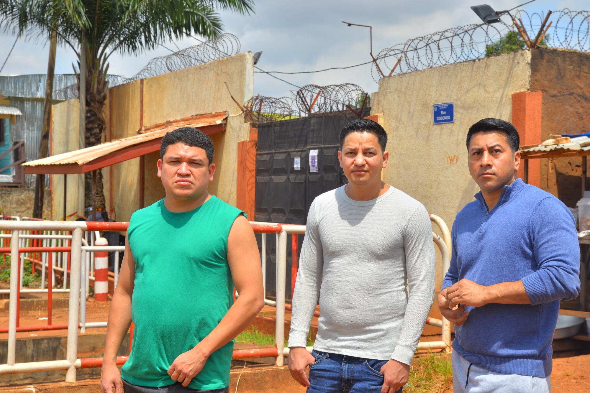 Three men appearing to be in their 30s stand in an urban area