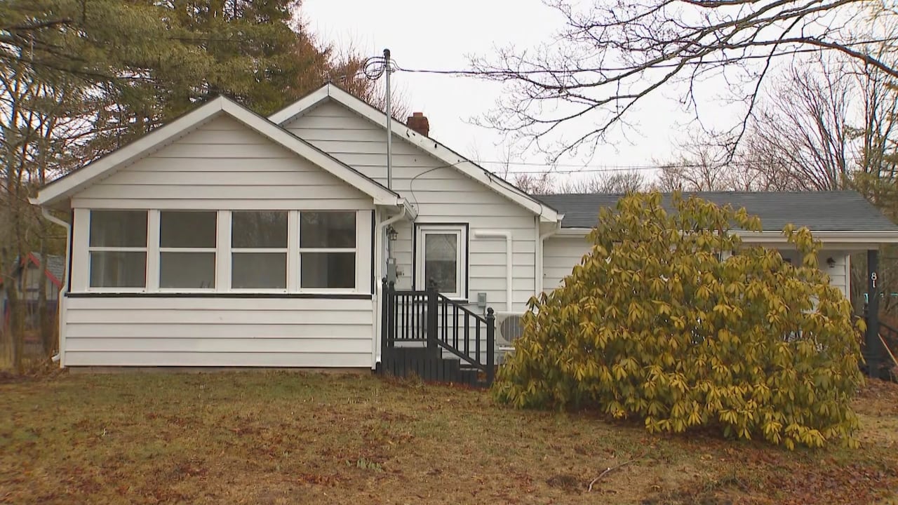 The front of a white house with a big bush in front of it with the leaves and grass turning burning.