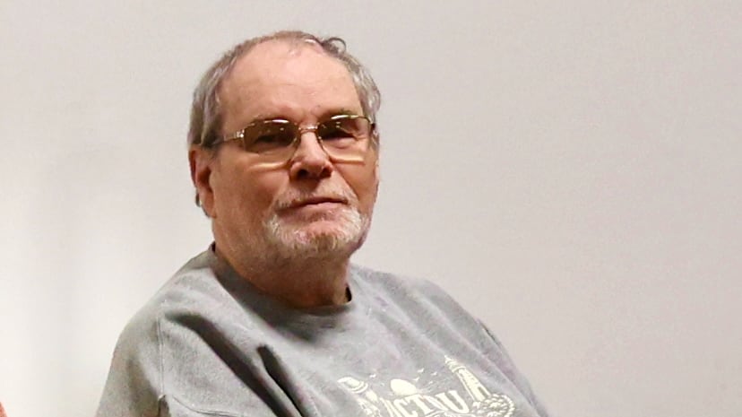 Douglas is looking at the camera with thin grey hair and glasses on.