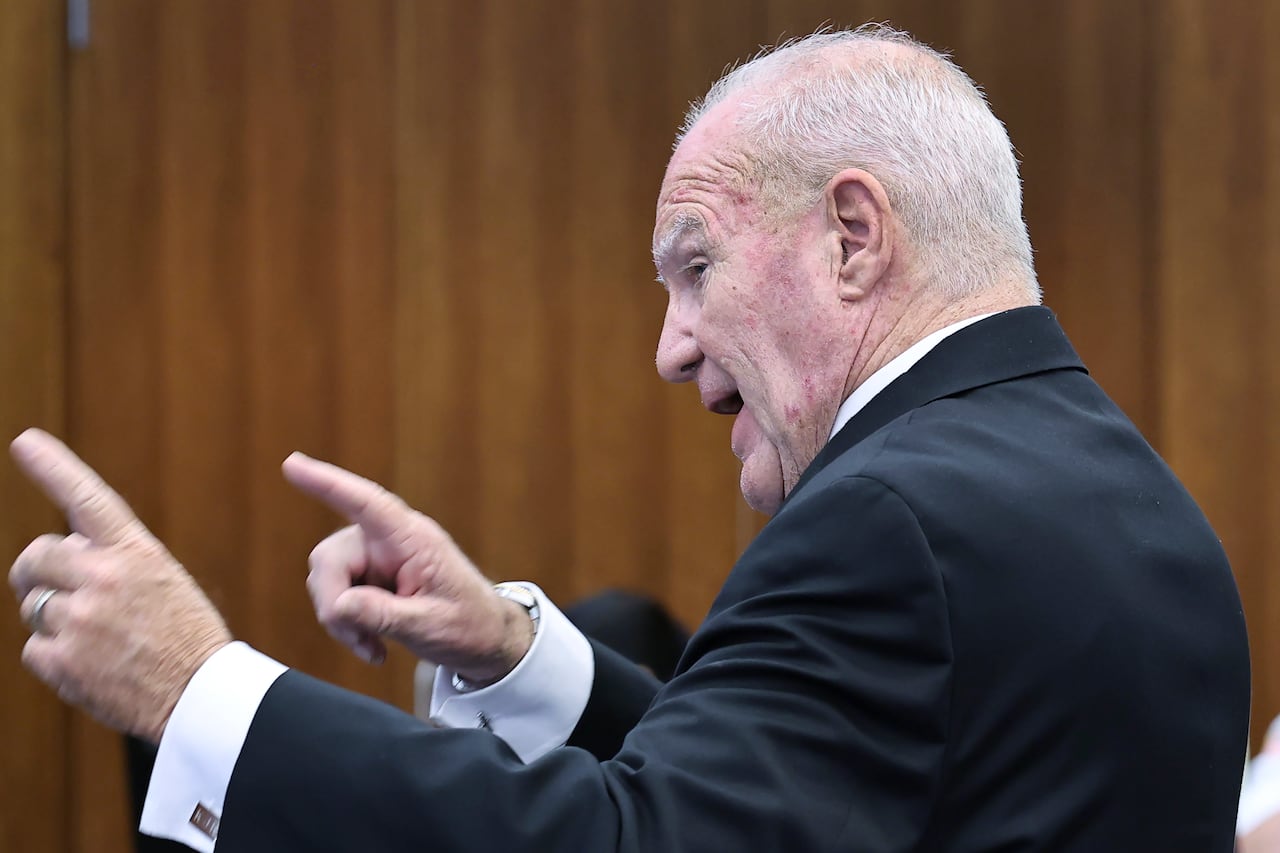 A side profile of an older man in a suit speaking