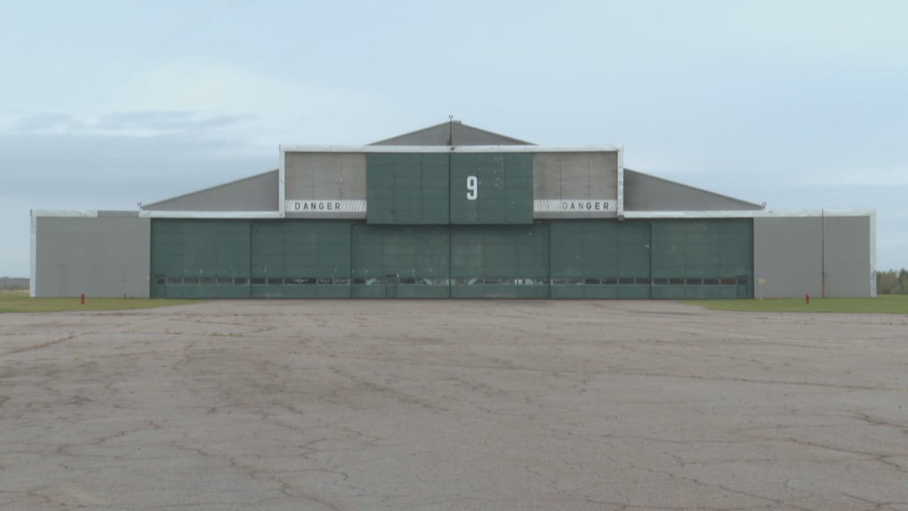 An old airplane hangar with two large bay doors is seen in an otherwise vacant lot.