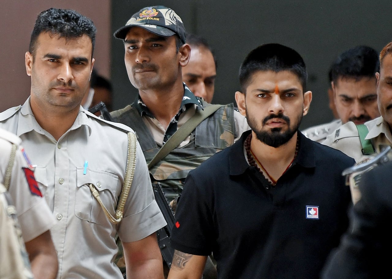 A man wearing a black T-shirt is escorted by police.