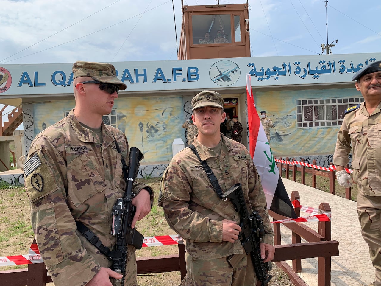 Apparent soldiers in caps and camouflage uniforms stand outdoors.