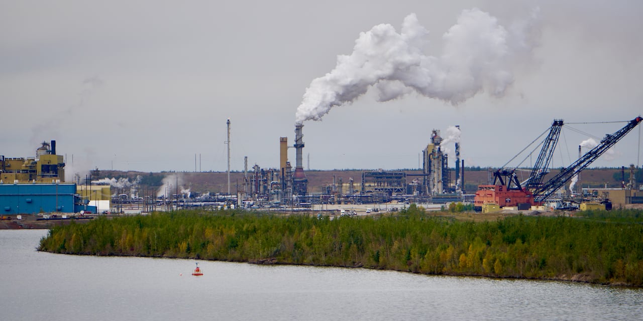 A lake is shown in the foreground with the industrial facility in the background and a forest in between.