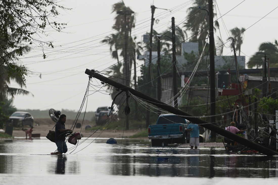 A man carries items through floodwater past downed electric lines after the passing of Hurricane Polo in Puerto San Carlos, Baja California Sur state, Mexico, Tuesday, Sept. 29, 2026.