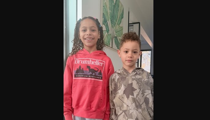 A young girl and boy stand shoulder to shoulder.