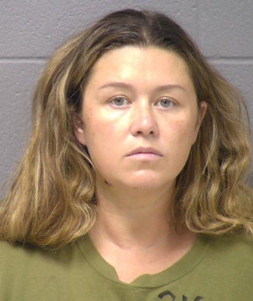 Mugshot of a woman with long, light brown wavy hair, wearing a green shirt, looking directly at the camera with a neutral expression.