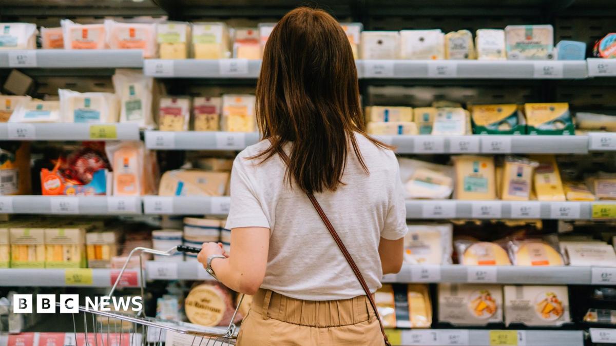 A woman from behind holding a shopping basket while looking at the cheeses on offer in a supermarket