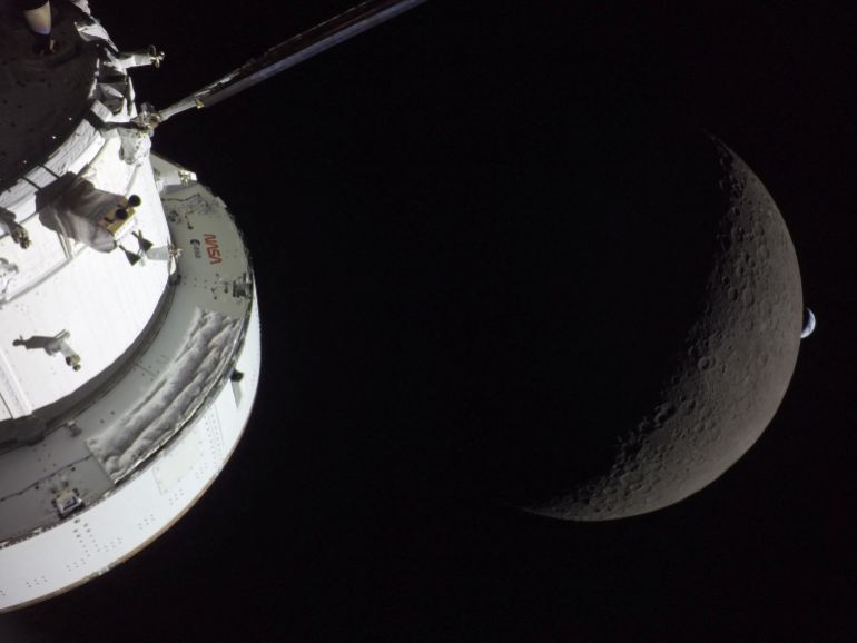 A view of NASA’s Orion spacecraft in the foreground, lit up by the sun as the moon and Earth are visible behind it as photographed by one of the cameras on the Orion spacecraft’s solar arrays during the Artemis II crew’s flyby of the moon on April 6, 2026