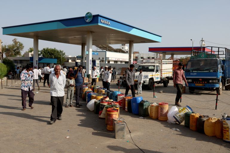 Villagers stand near plastic containers at a fuel station to fill their water pumps, as India faces rising oil prices, in Halvad, Gujarat, India
