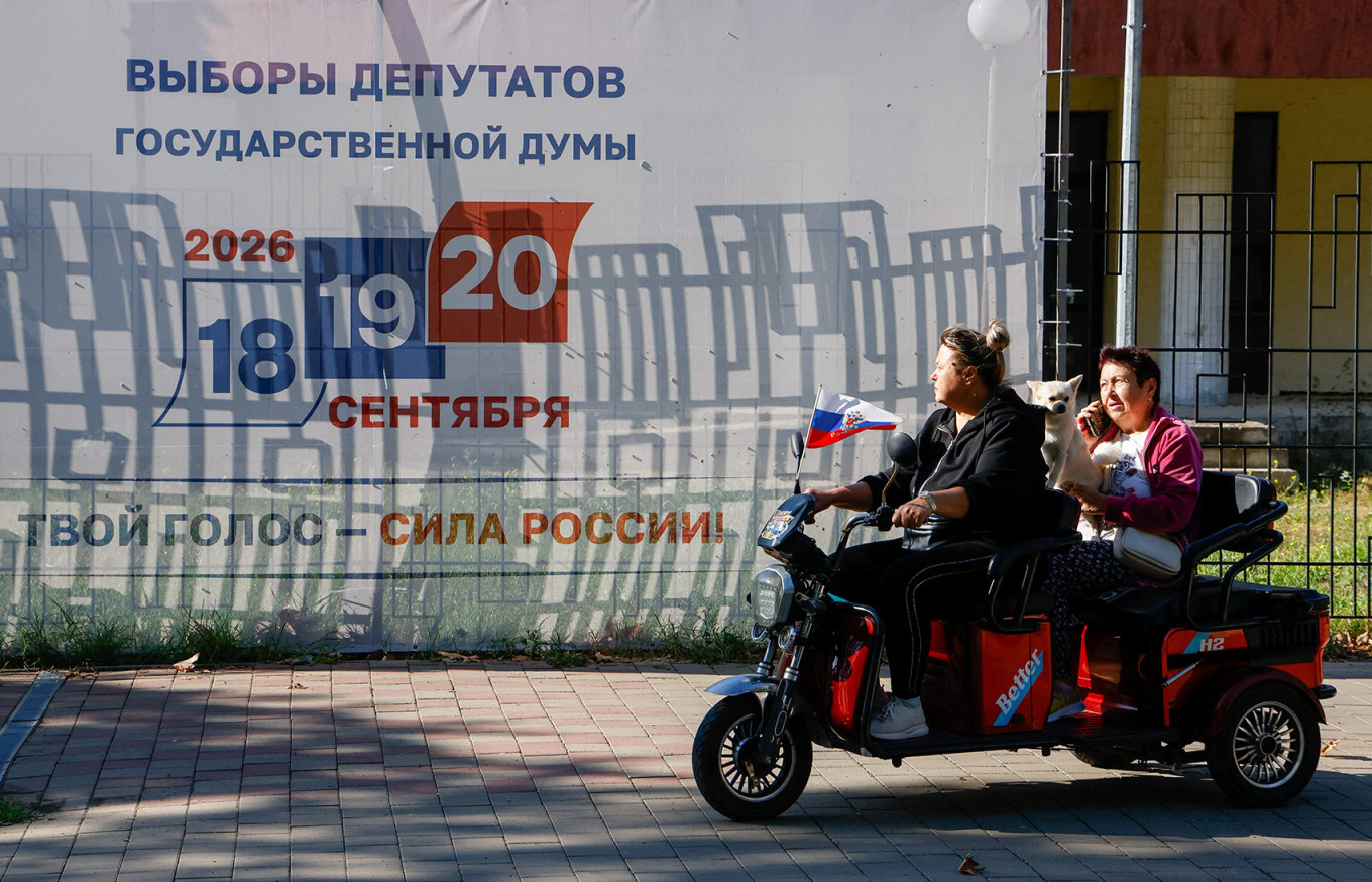 
					Women with a dog ride an electric motorcycle past a banner promoting Russia's parliamentary elections in Saki, annexed Crimea.					 					REUTERS / Alexey Pavlishak				