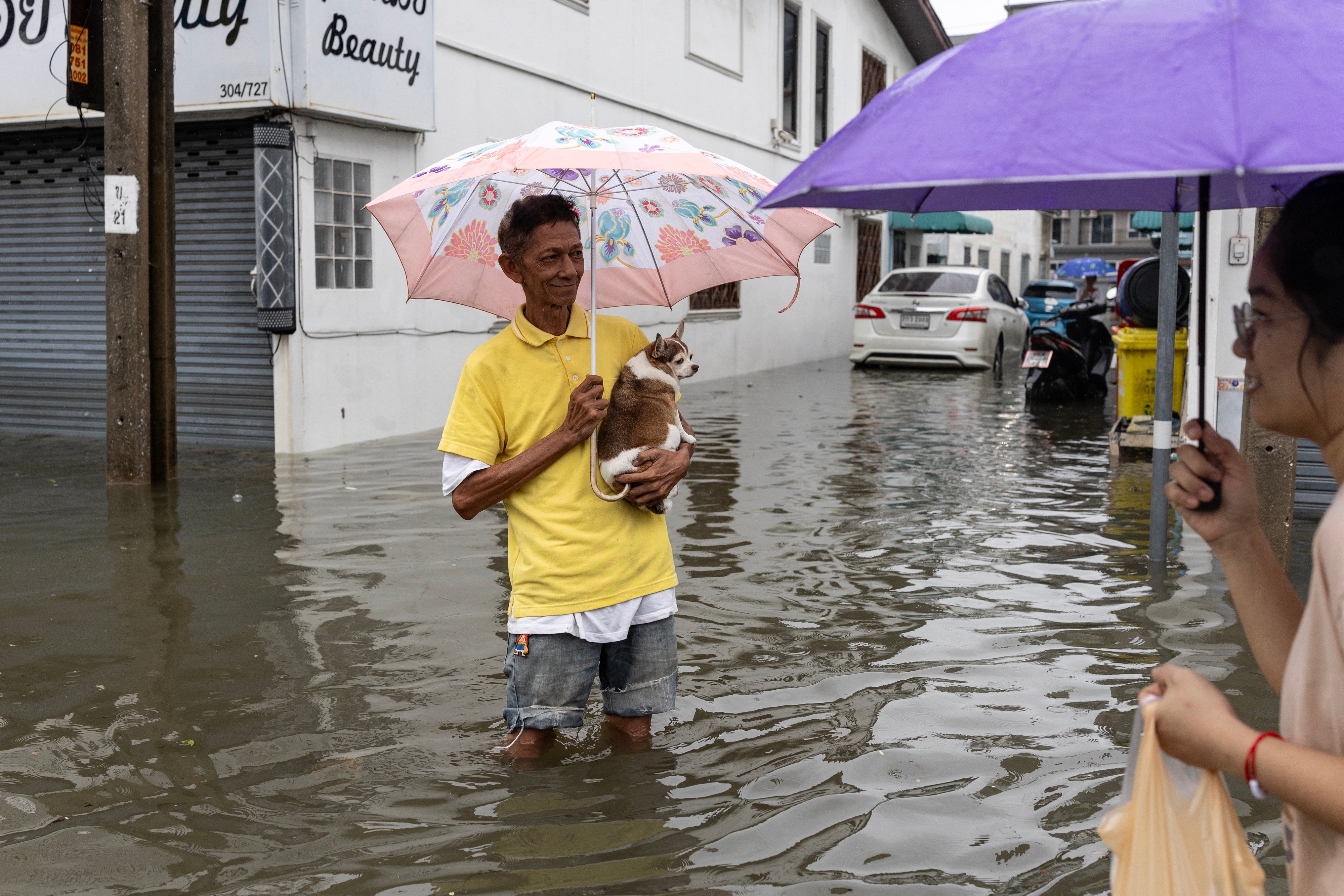 A man holding a small dog wades through floodwaters in the Bang Bua district of Bangkok on September 26, 2026