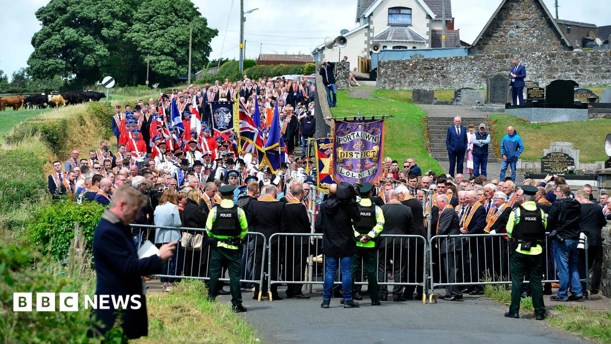 A large procession of Orange Order members being blocked by police from walking down a road.