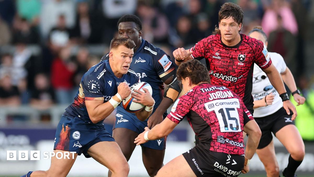 Joe Carpenter (left) of Sale runs towards Bristol's Tom Jordan (JORDAN 15) with other players from each side watching on