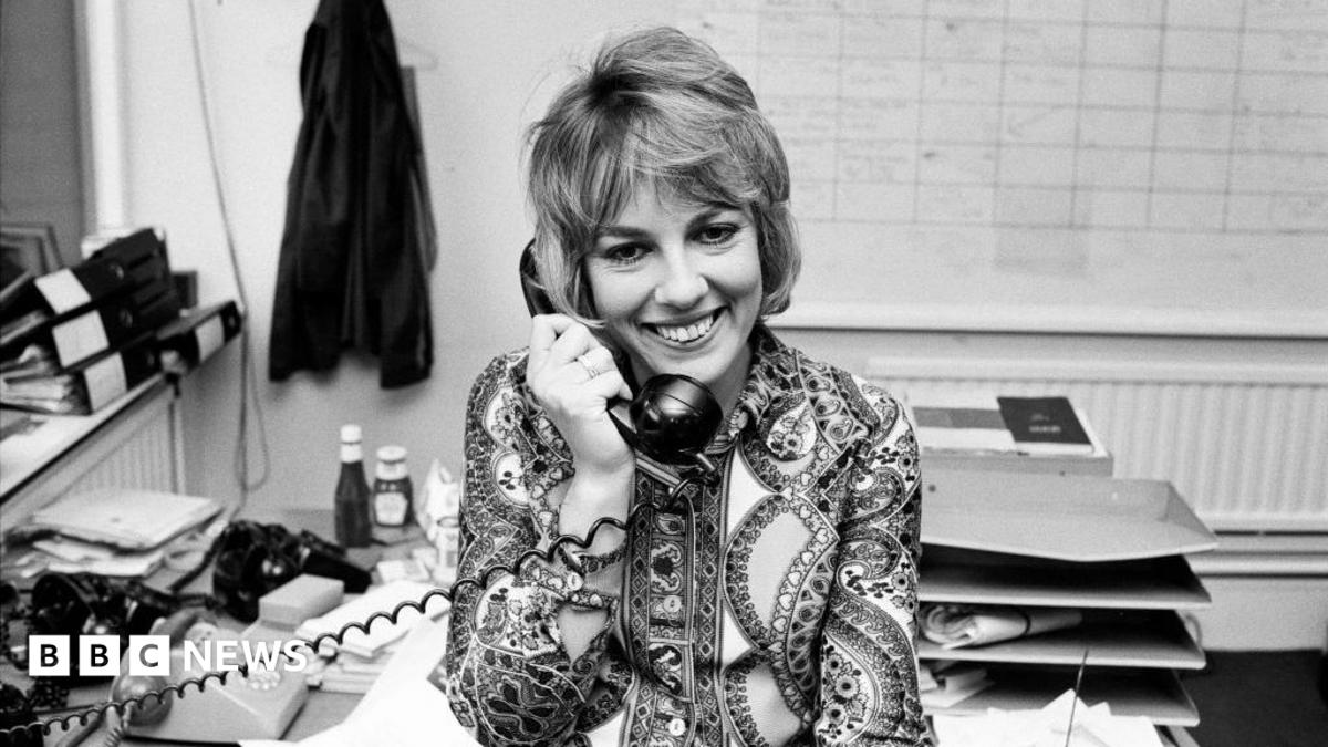 Esther Rantzen appears in a recent picture. She is smiling and dressed in a blue jacket with a matching feather in her hair.