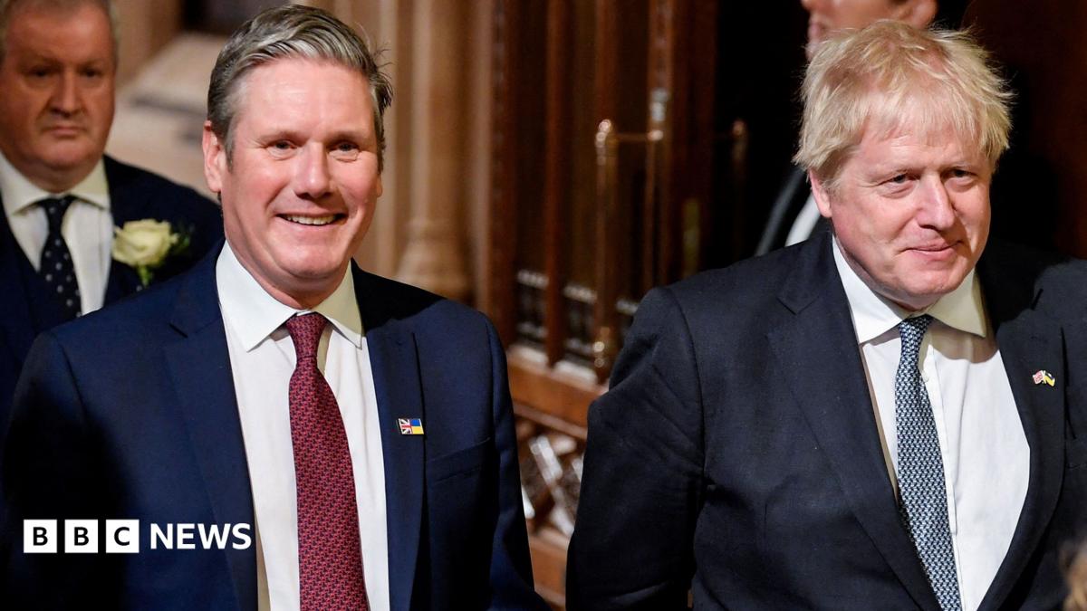 Keir Starmer on the left, and Boris Johnson on the right, walking together in the Houses of Parliament in 2024. They are smiling and both wear white shirts, a lightly patterned tie, and blue suit jackets.