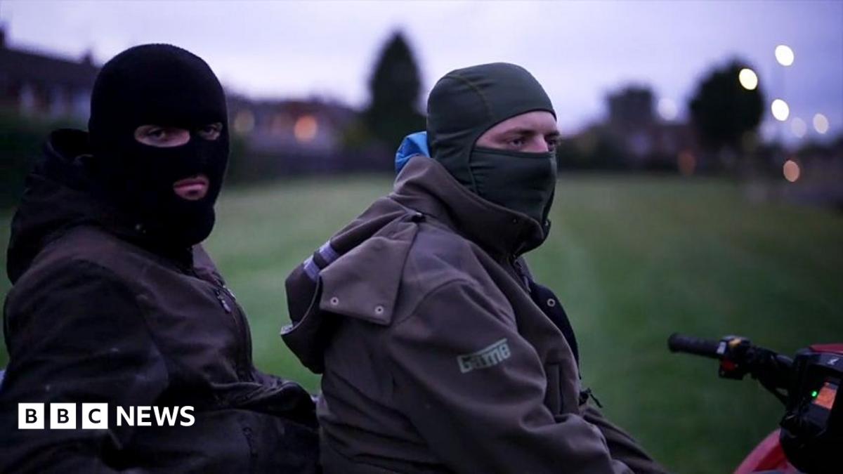 Two young men wearing balaclavas sit on a red quad bike