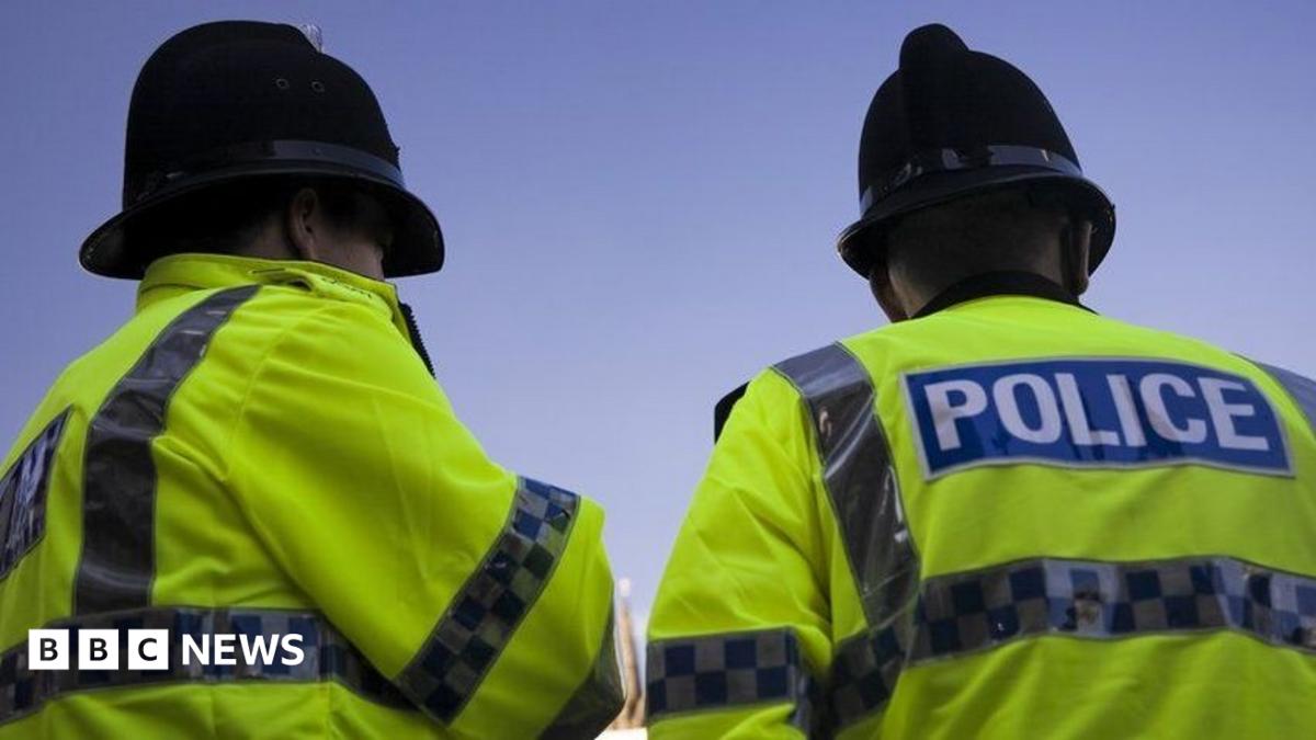 A stock image of two police officers from a low angle. They are facing away form the camera. They have high visibility coats on showing the work police and are wearing black police helmets.