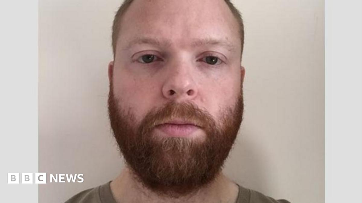 A police mugshot of Paul Chowles wearing a brown T-shirt and standing against a white background. He has a full beard and short red-brown hair, and is looking at the camera with a blank expression.