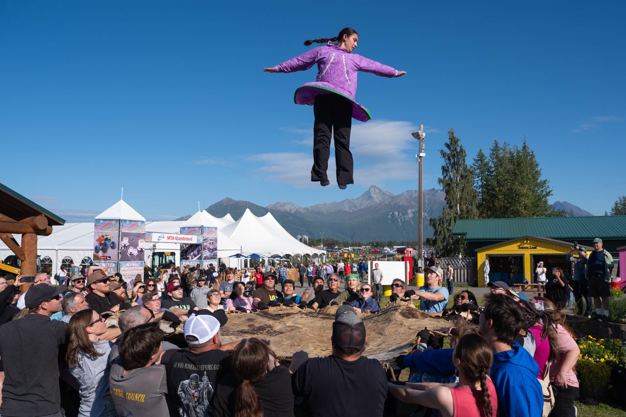 Daisy Vanblarcom, wearing a kuspuk, soars through the air during a blanket toss on Sept. 4, 2026 in Palmer, Alaska. The blanket toss is an Iñupiat tradition. As a state legislator in 1999, Mary Peltola started the tradition of state lawmakers wearing kuspuks on Fridays at the Capitol in Juneau.