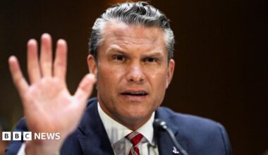 Pete Hegseth gestures by lifting his hand as he frowns
