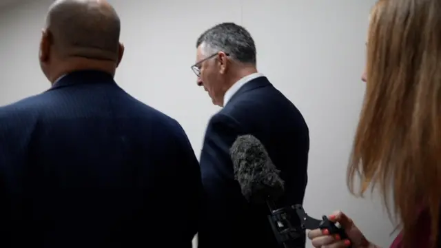 Gideon Saar and another man wearing a suit are pictured with their backs to the camera as a microphone is held towards them