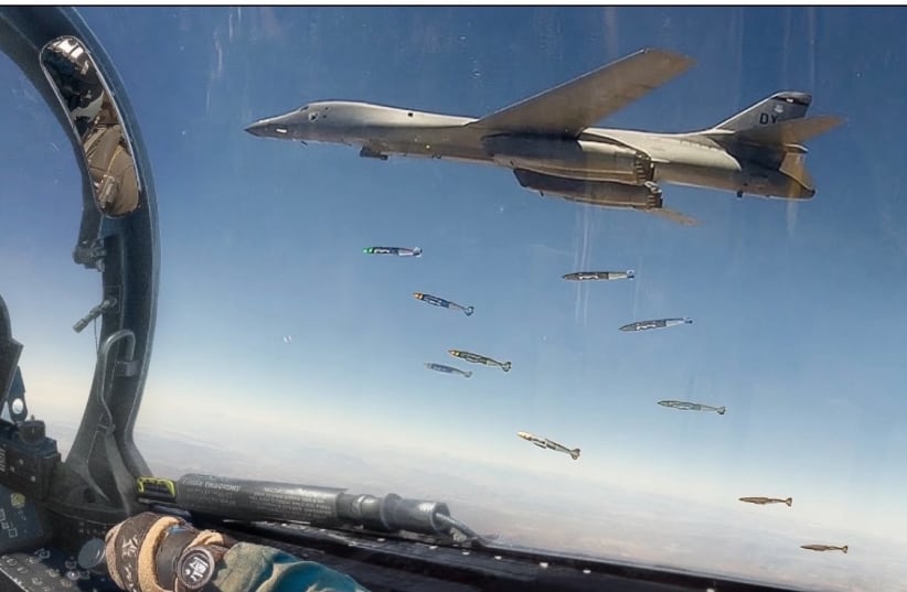 US Air Force Rockwell B-1B Lancer dropping JDAM bombs photographed from the canopy of an escort fighter jet.