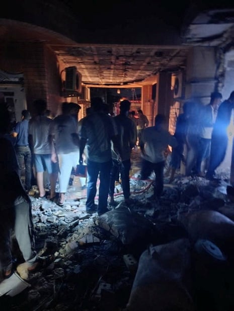 About a dozen people inside a damaged building in the semi darkness. 
