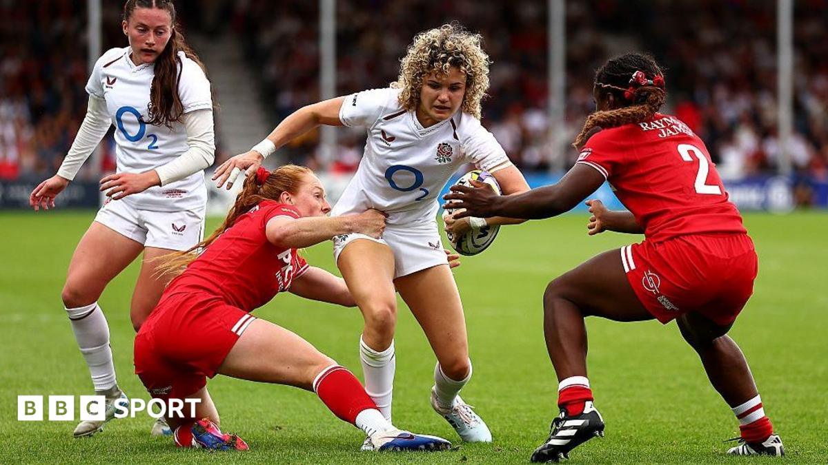 An England player, wearing white, is tackled by two Canada players in red
