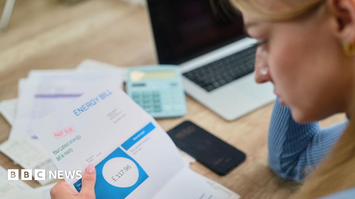 Woman looks at energy bill with paperwork, a calculator and a laptop on the table in front of her.