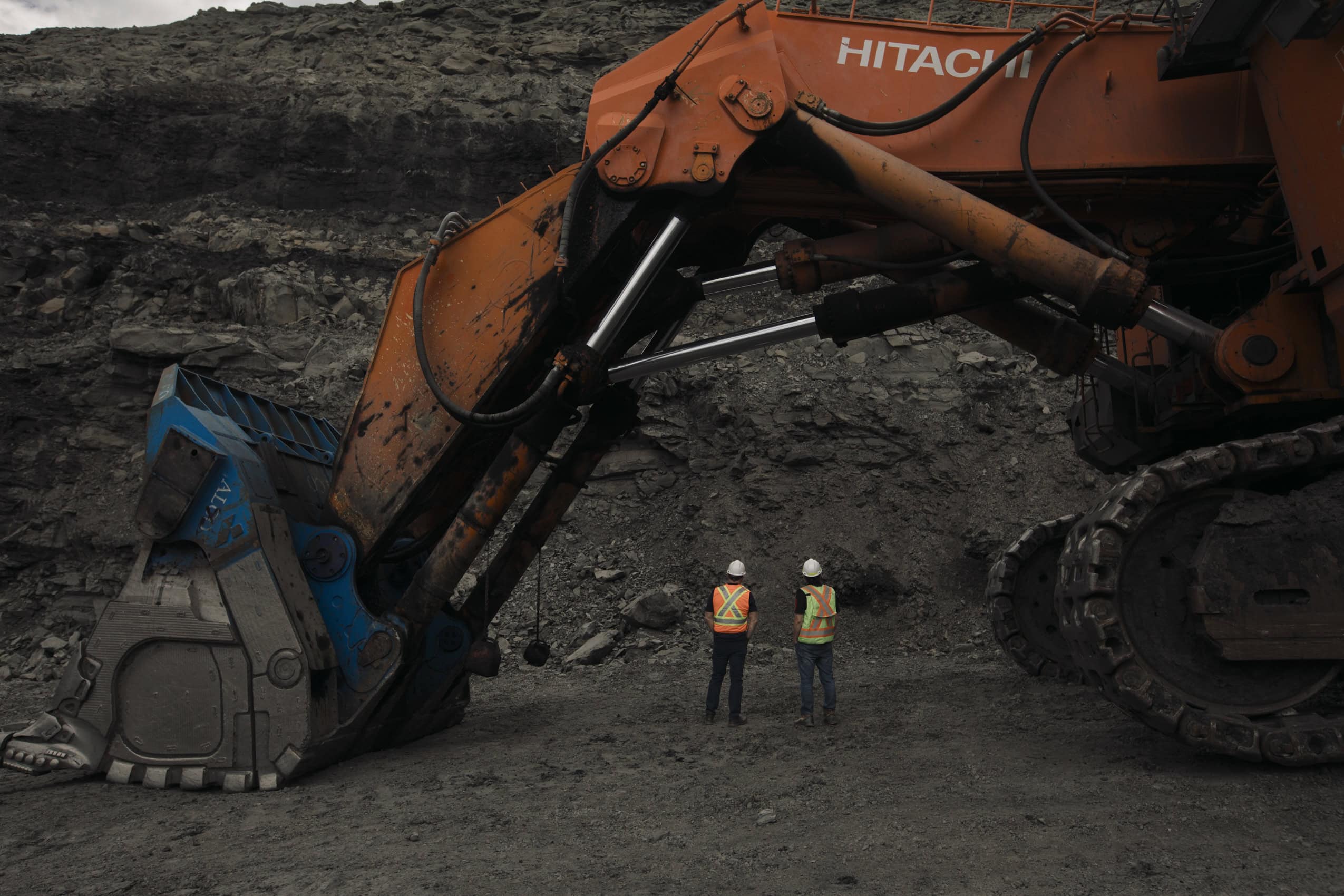 Two workers wearing hard hats and reflective vests stand under an excavator at the Coal Valley mine south of Edson, Alberta.