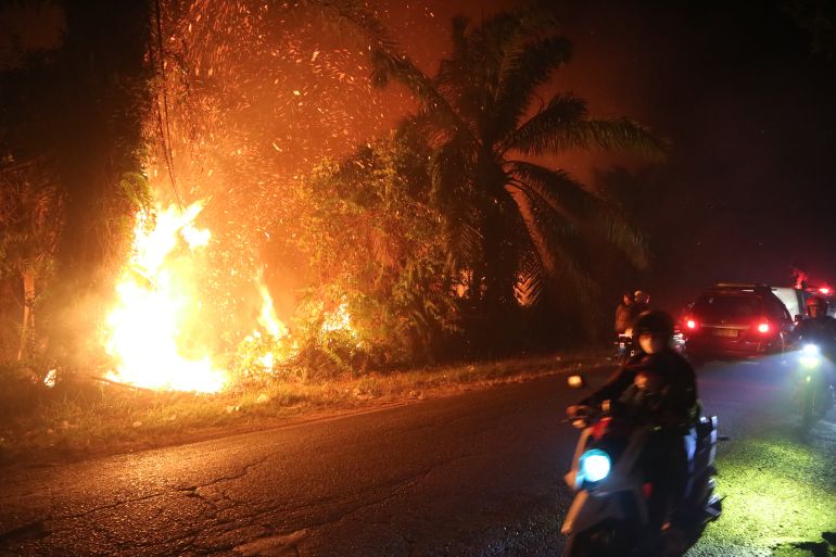 Motorists ride past a wildfire burning through a peatland field in Sampit, Central Kalimantan, Indonesia, on August 24, 2026