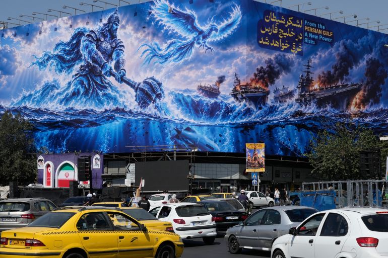 Vehicles drive past a billboard depicting a Persian legendary hero and flying figure hitting US aircraft carriers alongside a message in English: ‘From the Persian Gulf a new power rises’, and in Farsi, ‘The army of Satan will be drowned in the Persian Gulf’, at Islamic Revolution Square in downtown Tehran, Iran, Monday, September 14, 2026