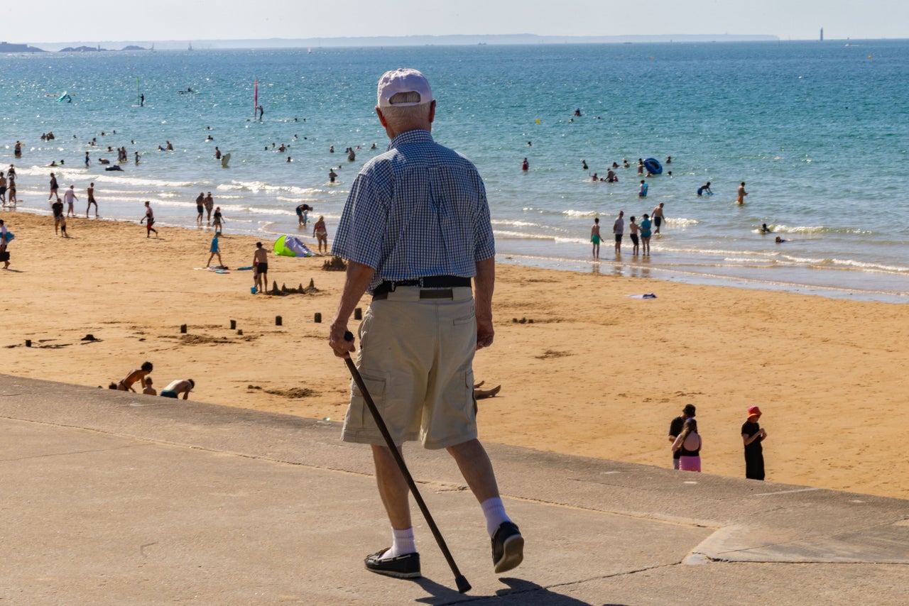 An elderly man walks with a cane, his gaze directed toward the sand (Hans Lucas/AFP via Getty Images)