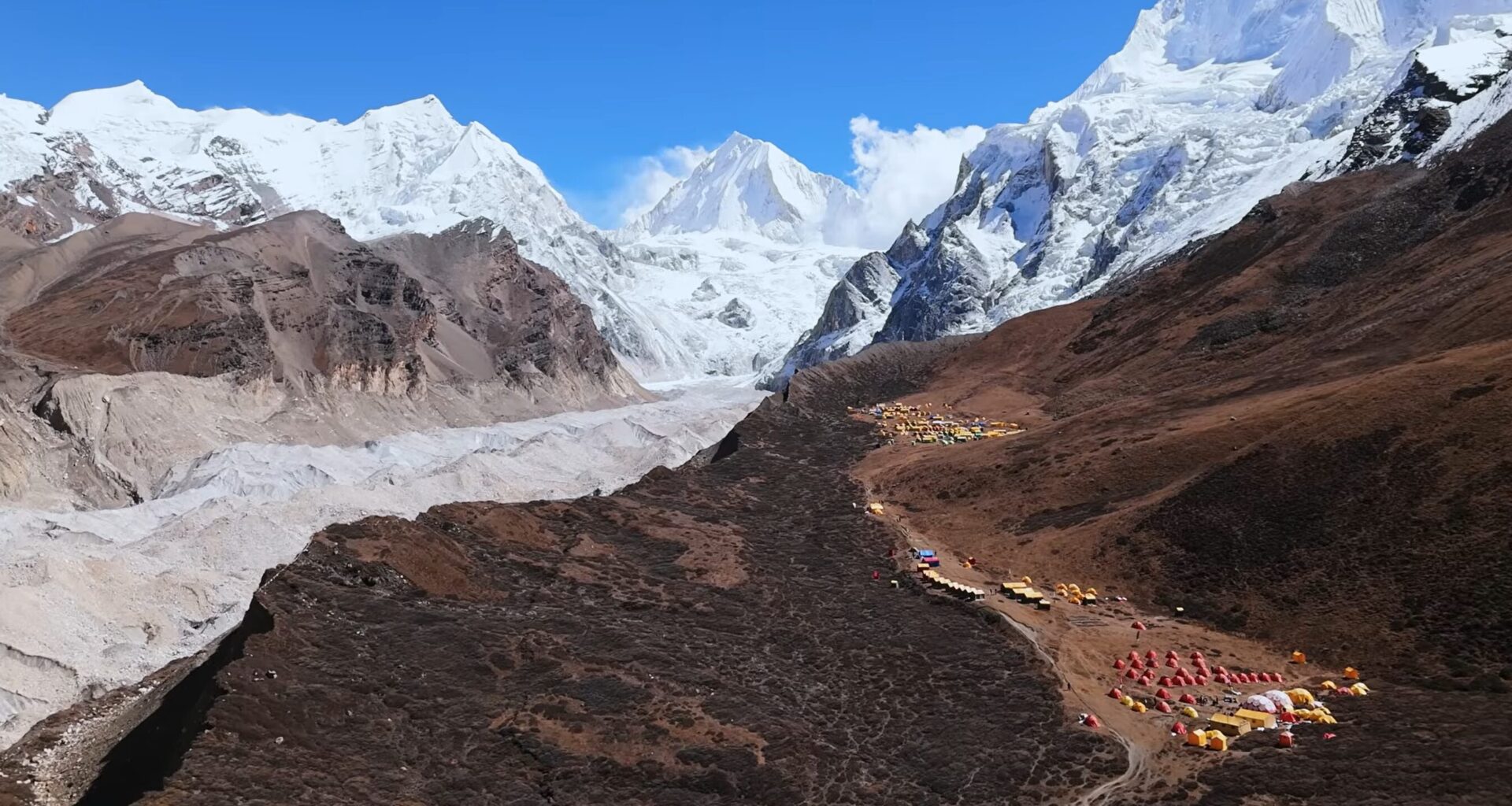 A stunning mountain scenery with a base camp built on dry ground and snowy peaks around.